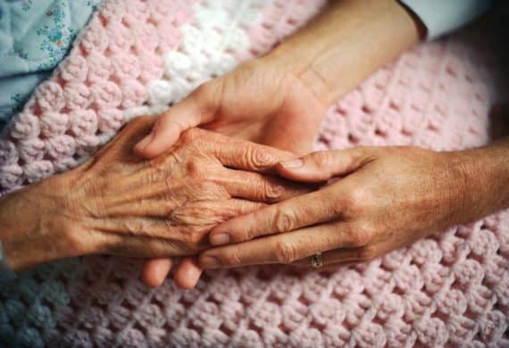 A caregiver holding hands with elderly woman